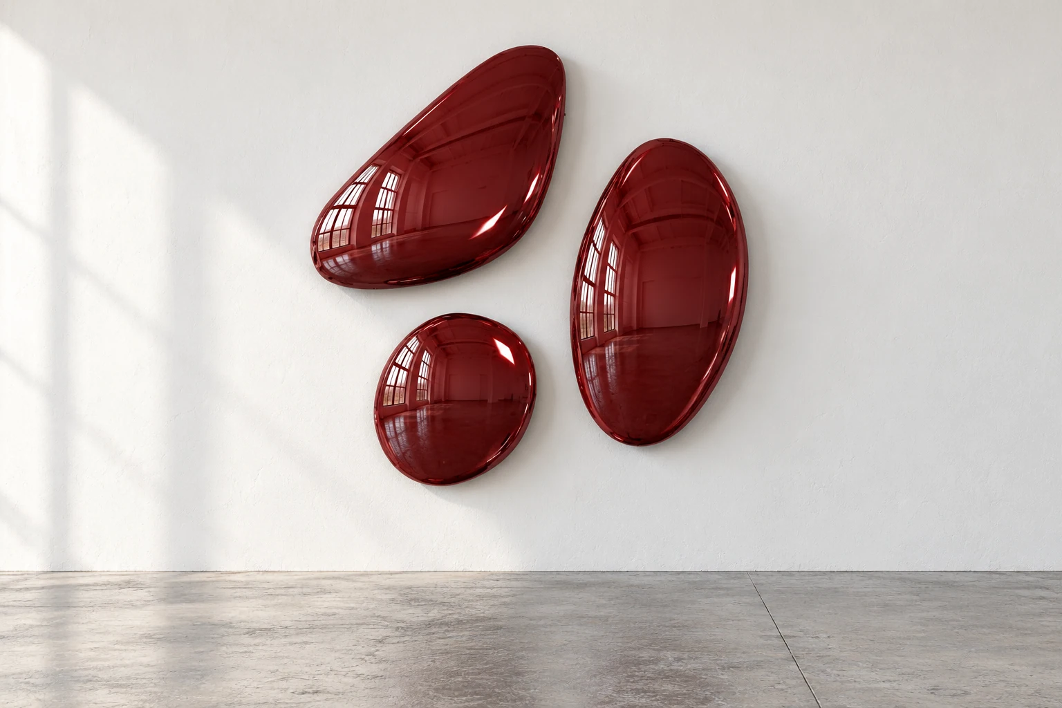 Three curved forms in oxblood, against a white wall above a grey concrete floor